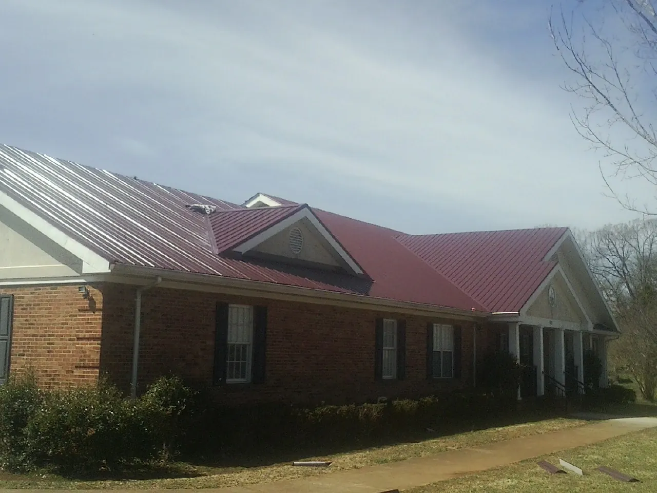 Red metal roof with gabled entries on a long brick building, from a Hail Damage Roof Repair job in Conover