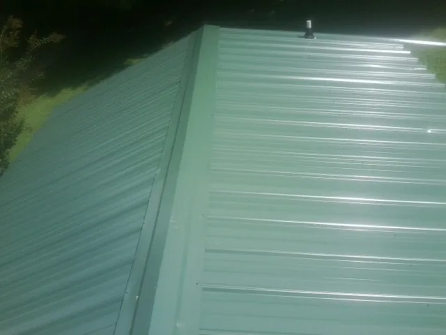 New green metal panels meeting at the ridge of a roof — Flat Roof Repair work by our crew in Conover