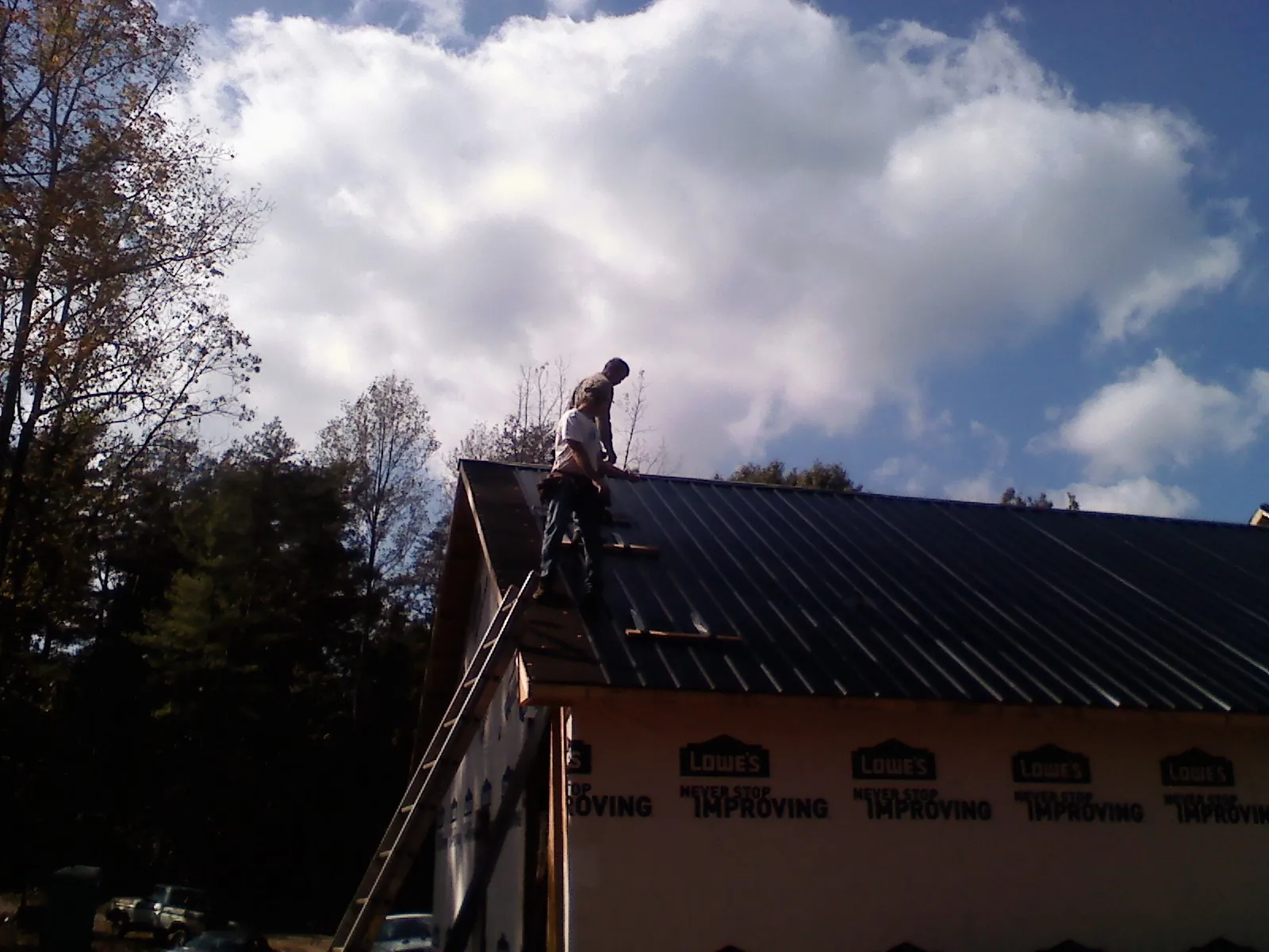Roofer fastening dark metal panels high against a cloudy sky, from a Roof Inspection job in Conover